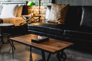 Un salón acogedor con una mesa de centro de madera, un sofá de cuero negro y una pared de ladrillo al fondo.