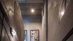 A narrow staircase with concrete walls and a ceiling, leading to a room with a framed abstract painting. - Samantan Hotel at Nimman (Chiang Mai)