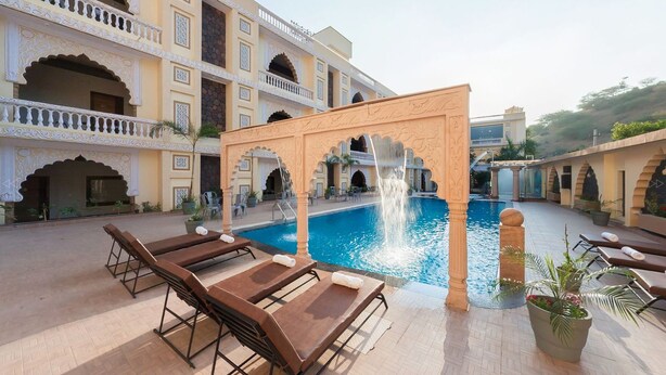 A pool area with sun loungers, a fountain, and a building with ornate architecture. - Pushkar City inn (Pushkar)