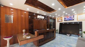 A reception area with a wooden reception desk, a TV mounted on the wall, and a sign indicating no smoking. - Pushkar City inn (Pushkar)