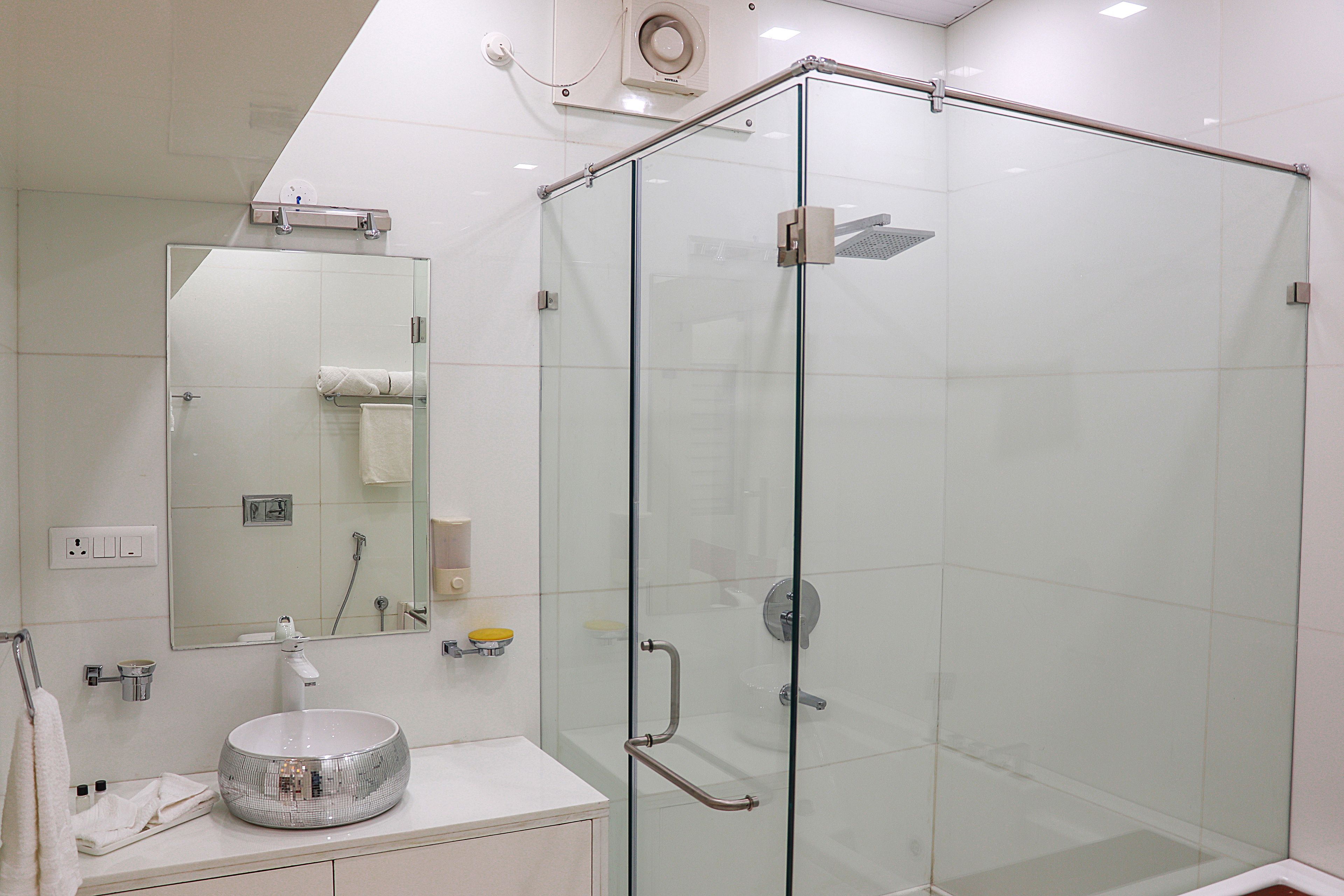 Un baño moderno con ducha de vidrio, espejo redondo y lavamanos blanco.