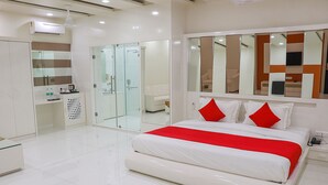 A modern hotel room with a large bed, a glass-enclosed walk-in closet, a vanity with a mirror, and a ceiling fan. - Pushkar City inn (Pushkar)