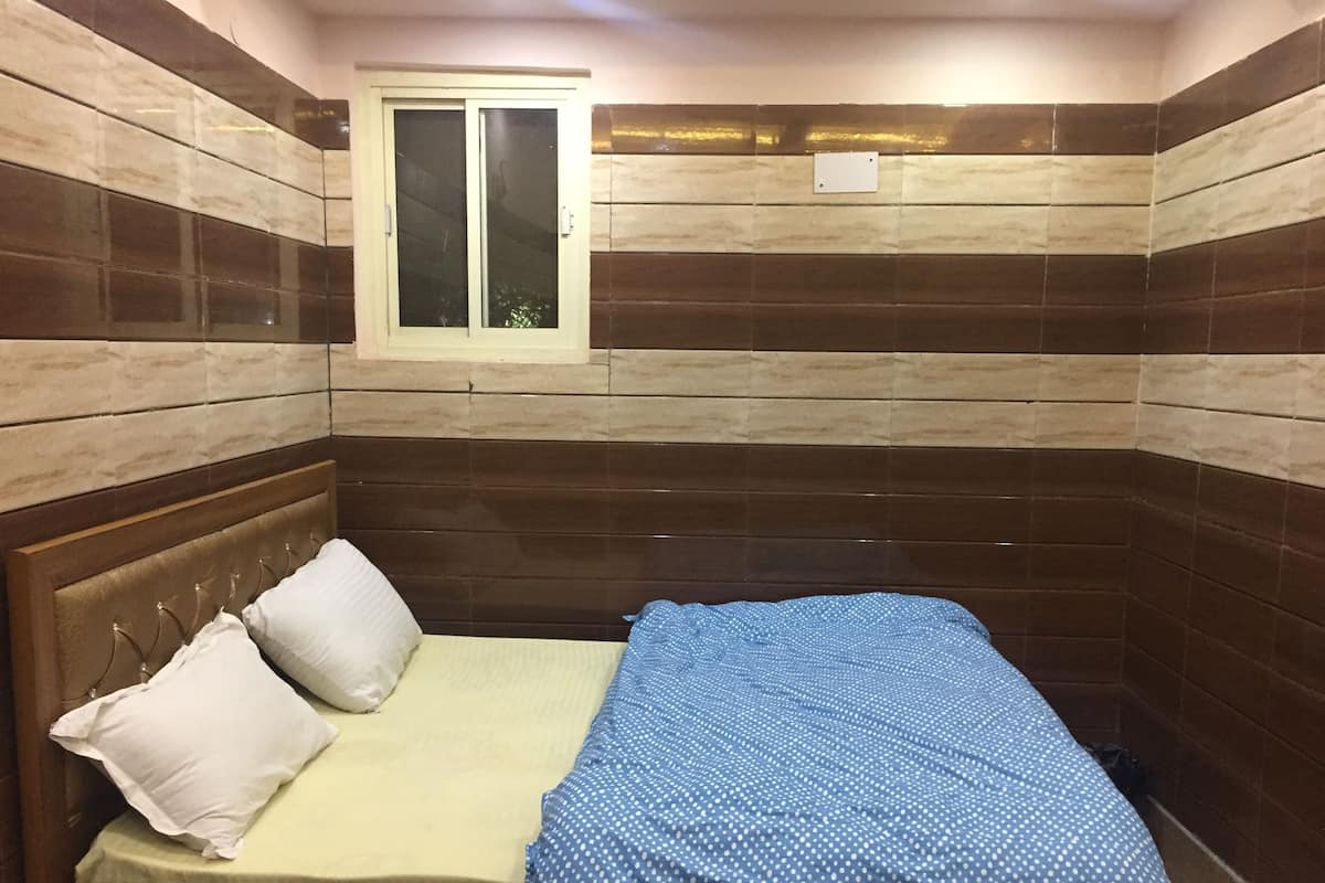 A small, single-bed room with a wooden headboard, two pillows, and a blue polka-dotted bedspread.