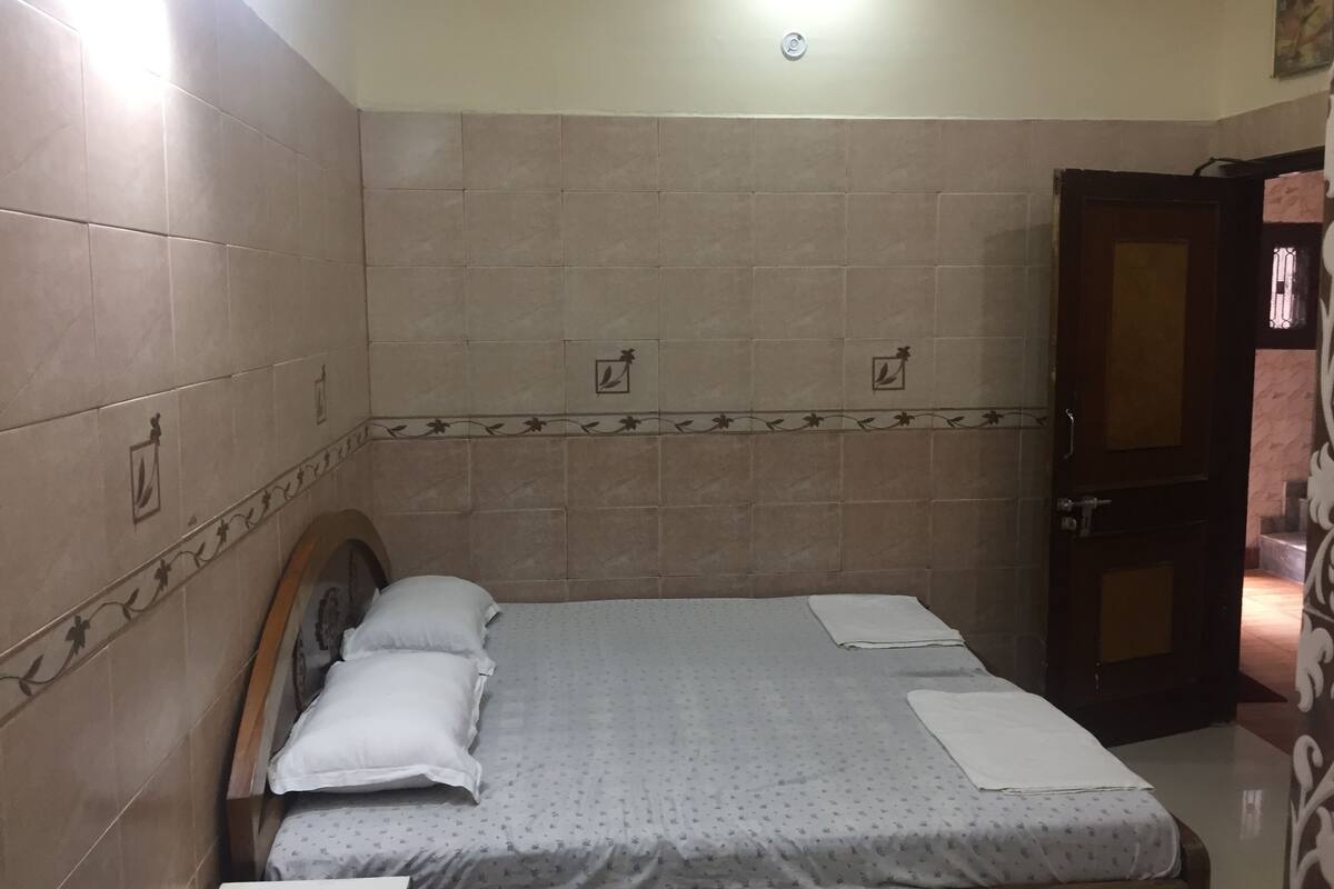 A small, neatly arranged bedroom with a single bed, a wooden headboard, and a door to the right.