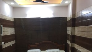 Une chambre à coucher avec un lit, un petit tabouret en bois, un canapé en cuir noir et un ventilateur de plafond.