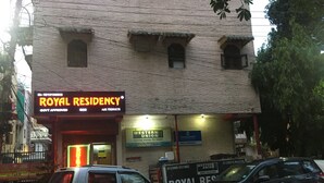 Un immeuble dont la façade porte une enseigne indiquant « ROYAL RESIDENCY » et « WESTERN UNION ». Deux voitures sont garées devant.