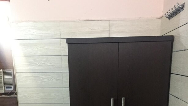 Une armoire en bois sombre, dotée de deux portes et de poignées, placée contre un mur orné d’un motif à carreaux noirs et blancs.