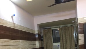 A room with a black leather sofa, a ceiling fan, and a window with curtains.