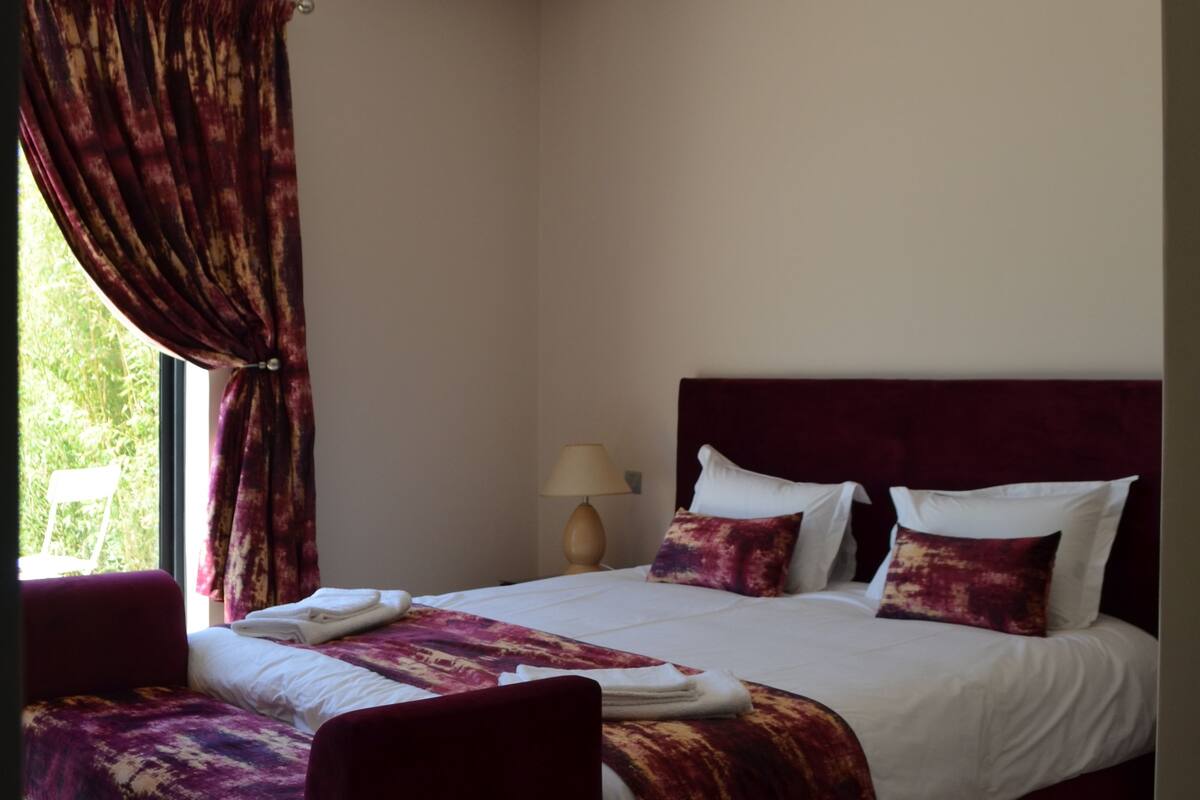 A bedroom with a bed, a window with curtains, and a nightstand.