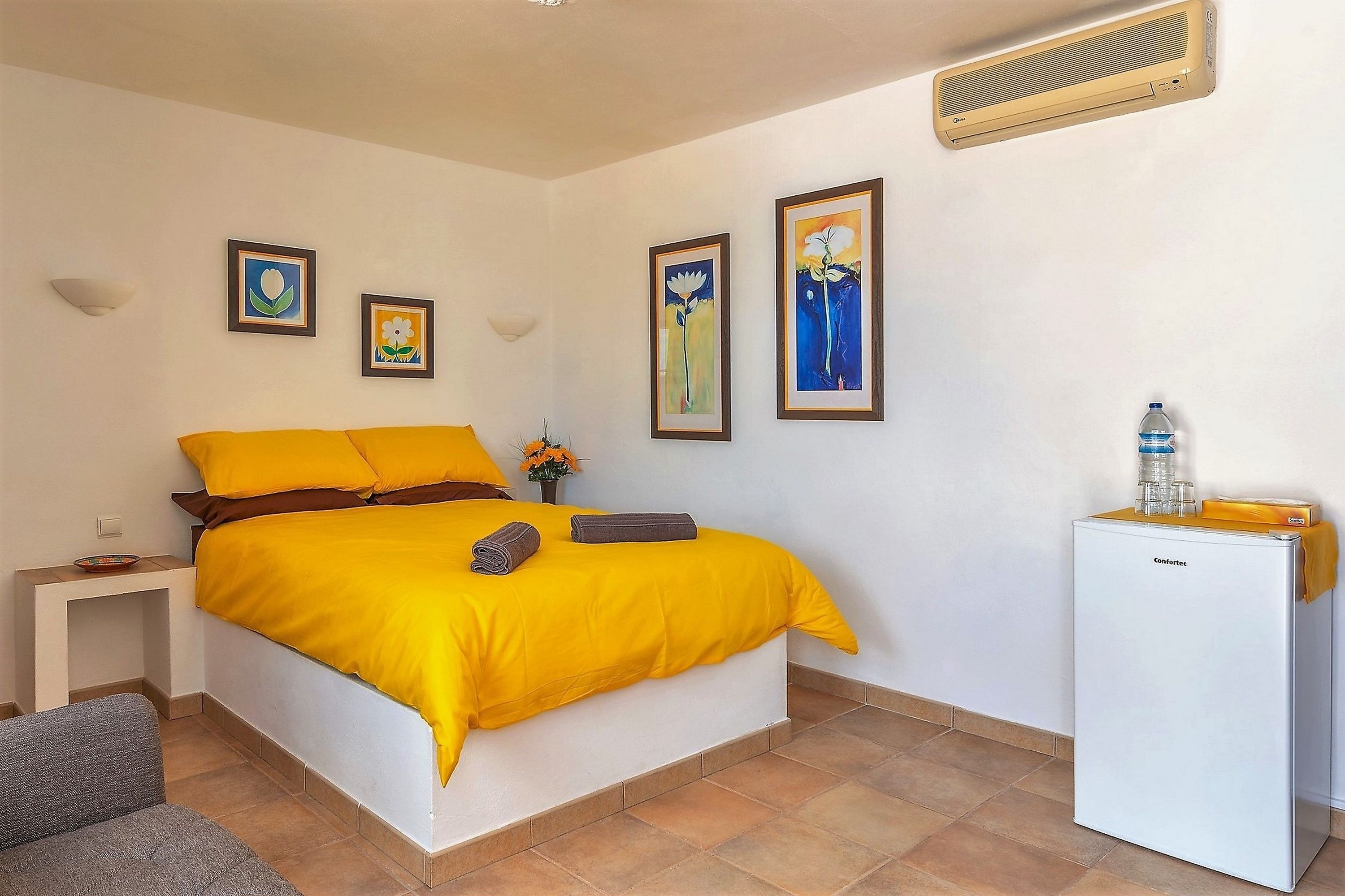 Ein Hotelzimmer mit einem Bett, einem kleinen Tisch, einem Stuhl, einem Wasserspender und einer Wandklimaanlage.