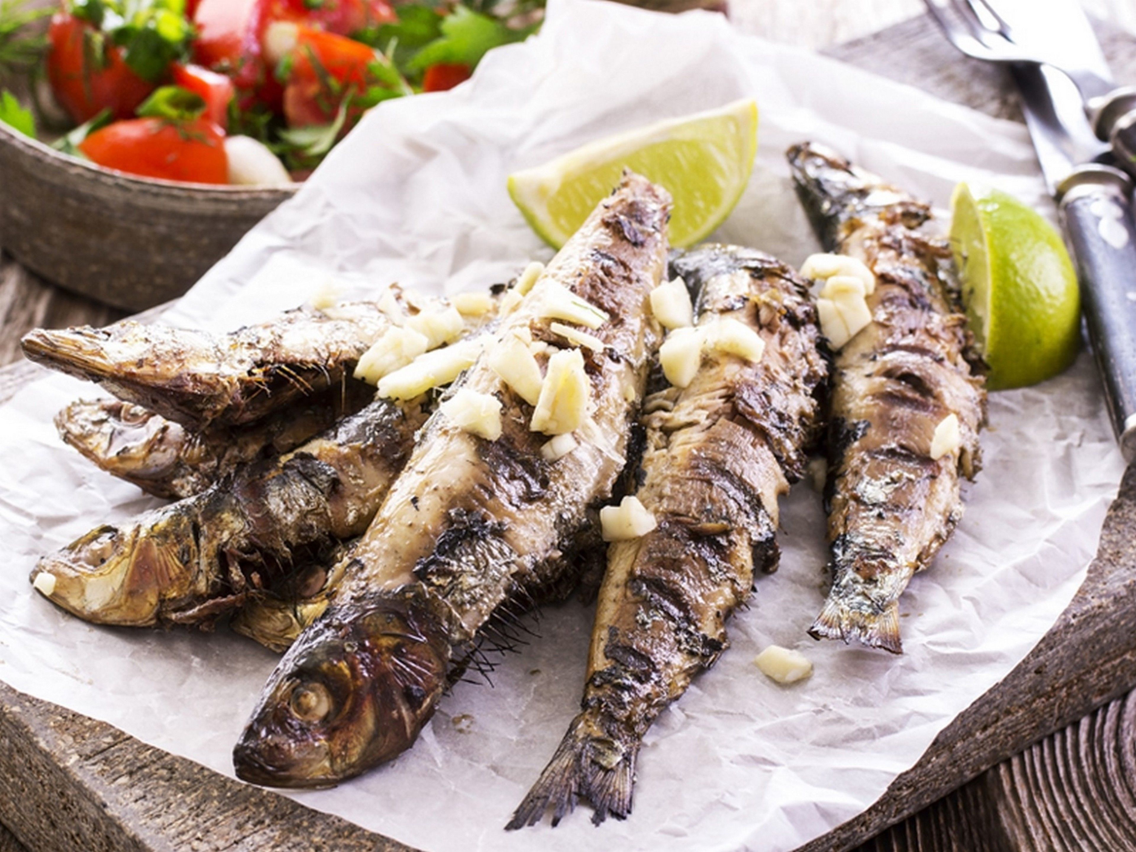 Grilled fish with garlic on a wooden board, accompanied by a lime wedge and a side salad.