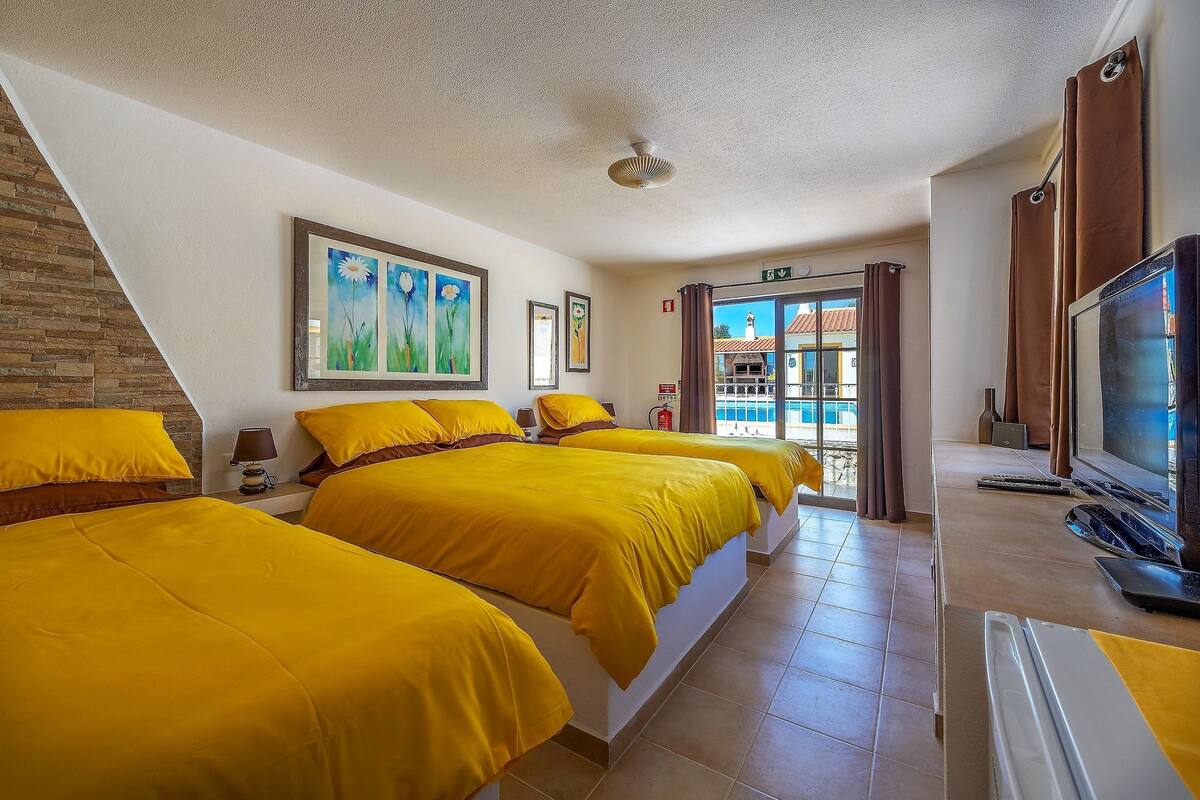 A hotel room with two beds, a TV, and a view of the outside.