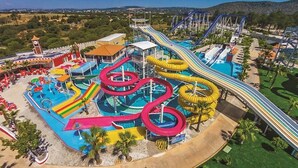 A water park with multiple slides and pools, surrounded by palm trees and a clock tower. - Casa dos Ninos (Silves)