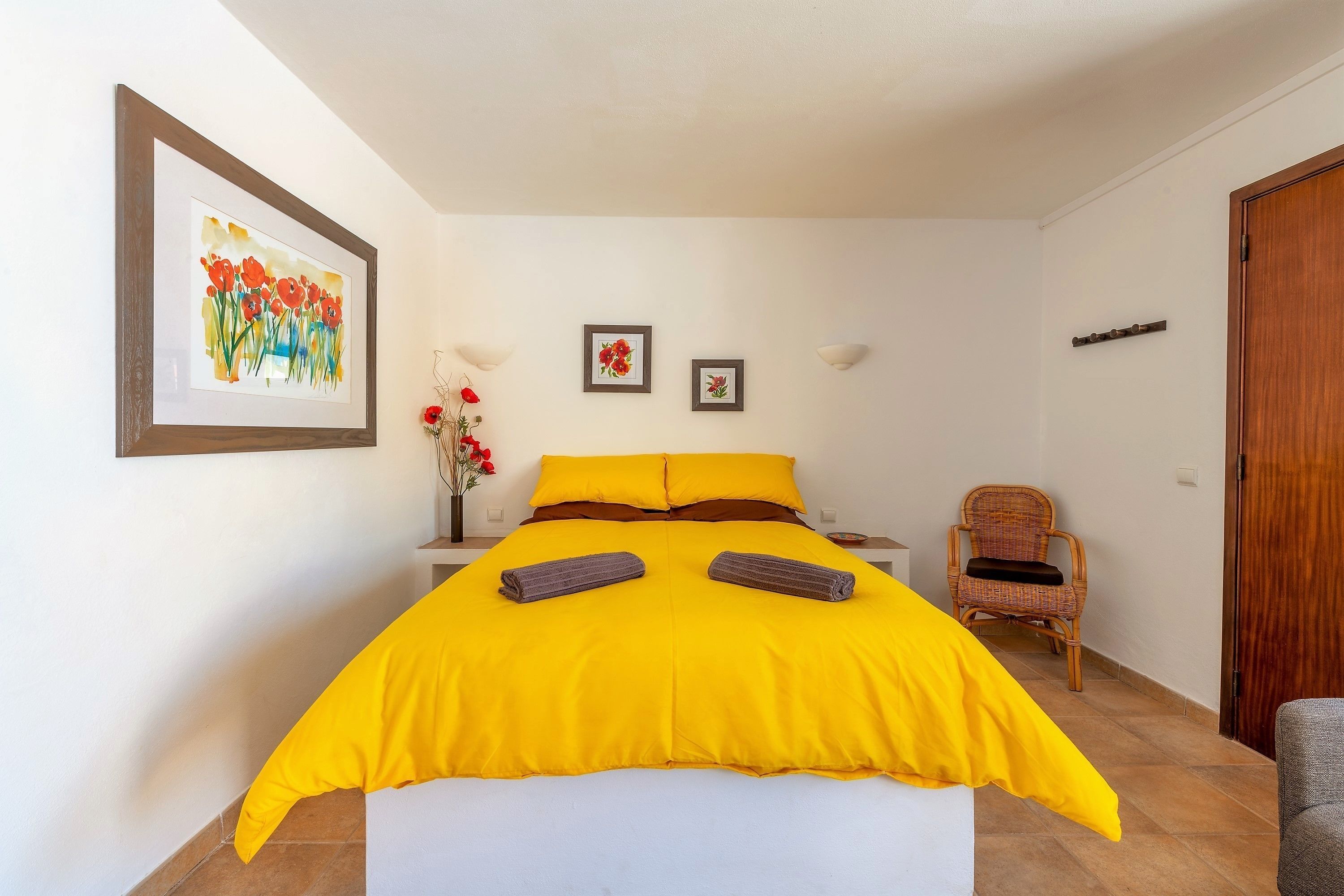 A bedroom with a bed, a chair, a nightstand, and a wall with framed pictures.