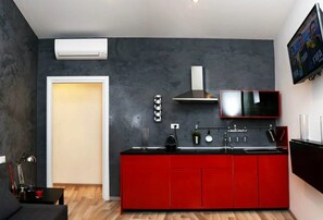 A modern kitchen with red cabinets, a black countertop, and a built-in stove. There is a TV mounted on the wall and an air conditioning unit above the door. - Guest house Roma (Rome)