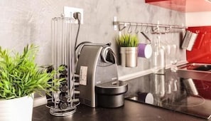 Une cuisine équipée d’une machine à café, d’un porte-ustensiles suspendu et d’une plante en pot.