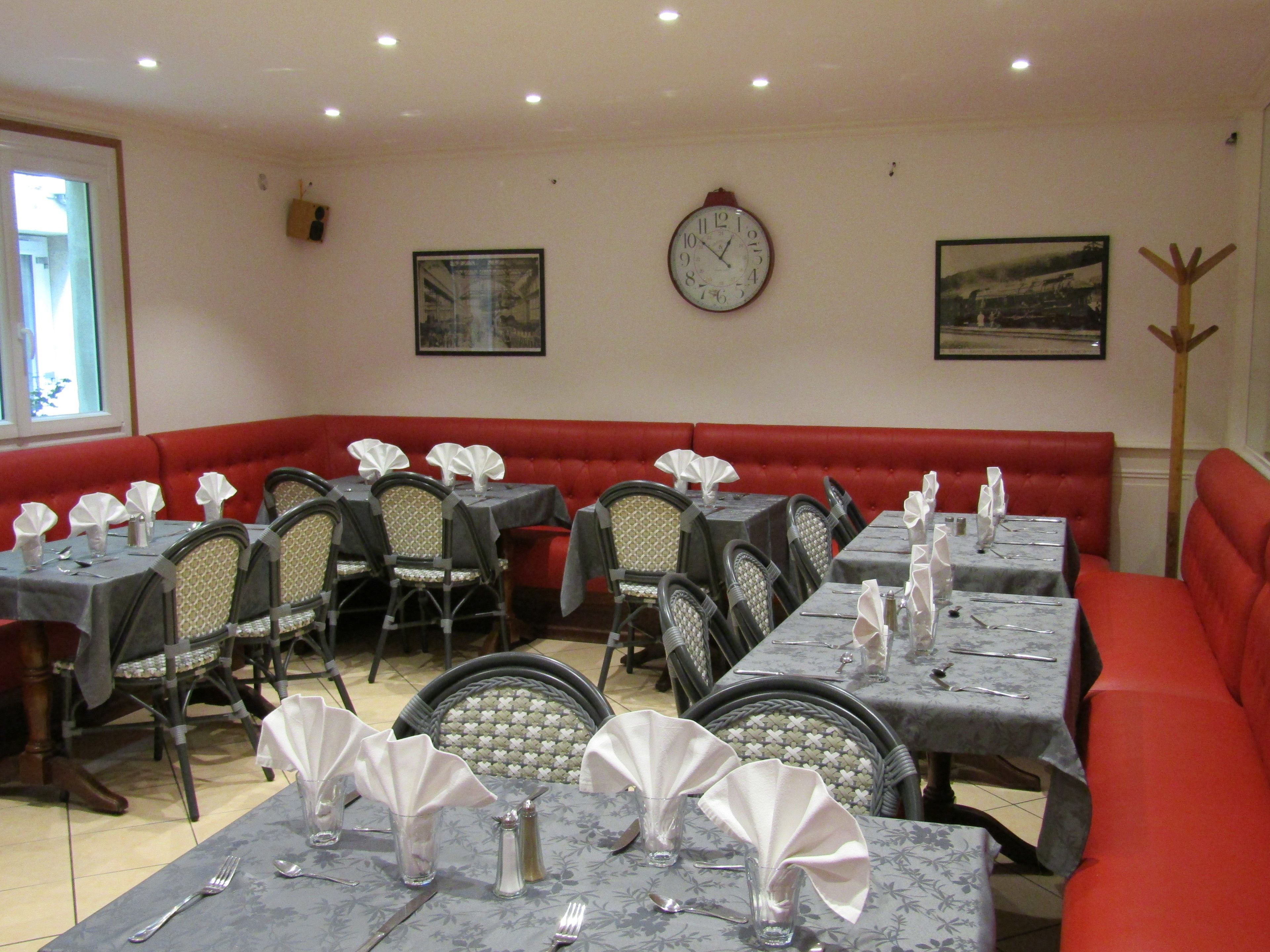 A restaurant with tables set for dining, red cushioned seating, and a wall clock.