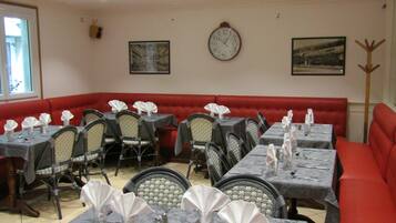 A restaurant with tables set for dining, red cushioned seating, and a wall clock.