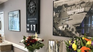 A reception area with a clock, a framed photograph, and two vases with flowers on a counter. - Le Creusot Hôtel (Le Creusot)
