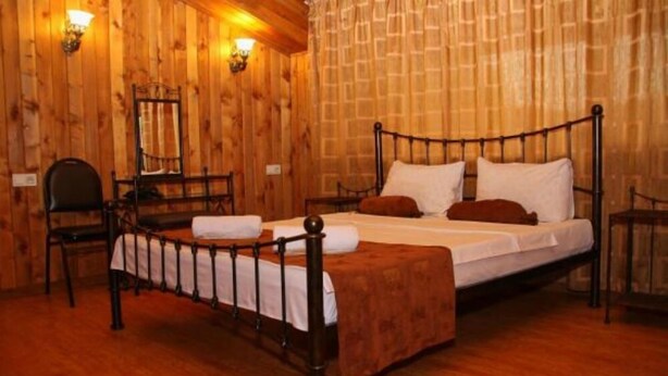 A wooden-paneled room with a single bed, a chair, and two wall-mounted lamps.
