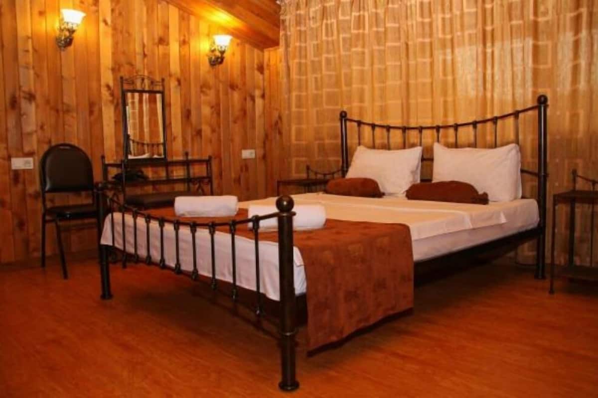A wooden-paneled room with a single bed, a chair, and two wall-mounted lamps.