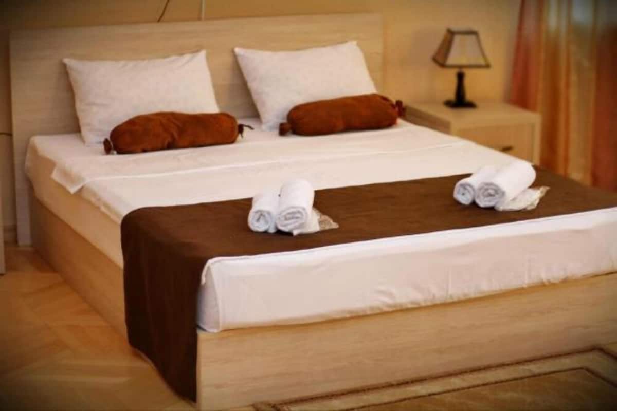 A neatly made bed with white and brown bedding, a wooden headboard, and a small bedside table with a lamp.