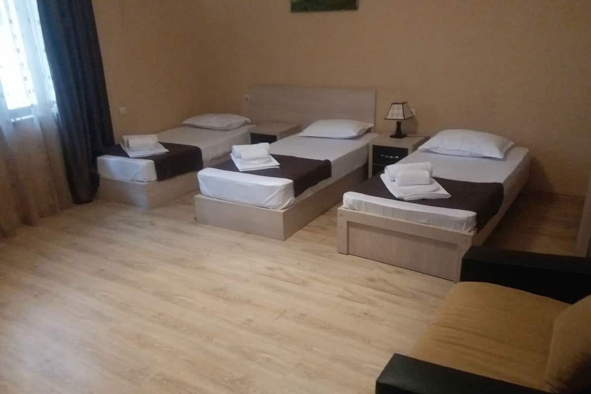 A hotel room with three beds arranged in a row, a small table, and a chair.