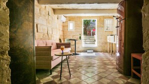 A cozy room with a stone wall, a pink sofa, a small table with a glass of orange juice, and a view of a staircase leading outside. - House of Pomegranates (Sliema)