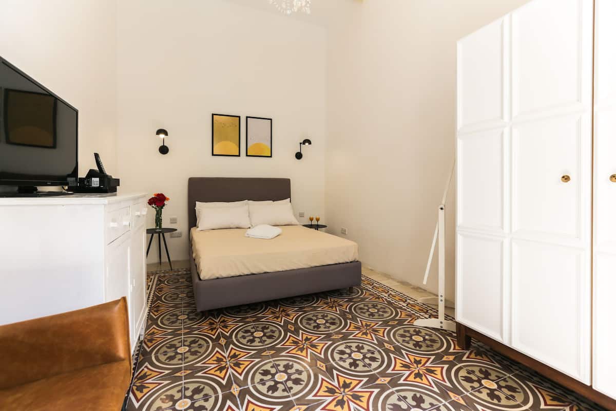 Un dormitorio con cama, televisor, escritorio, silla, armario y piso estampado.