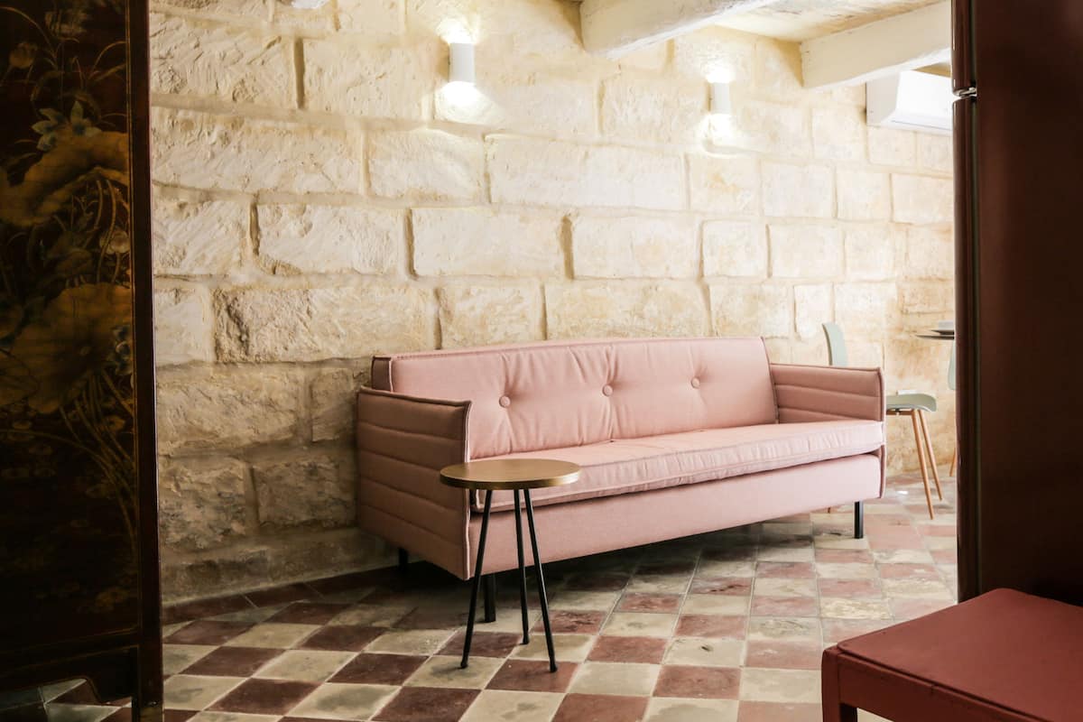 Una habitación con un sofá rosa, una mesita redonda pequeña y un suelo a cuadros.