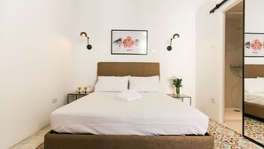 A neatly made bed with white linens, a brown headboard, and a patterned floor. - House of Pomegranates (Sliema)