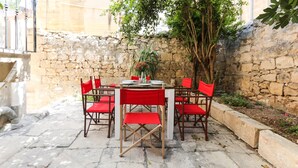 An outdoor patio with a stone wall, a round table with red chairs, and a potted plant. - House of Pomegranates (Sliema)