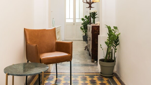 A hallway with a checkered floor, a brown leather chair, a small table, and a potted plant. - House of Pomegranates (Sliema)