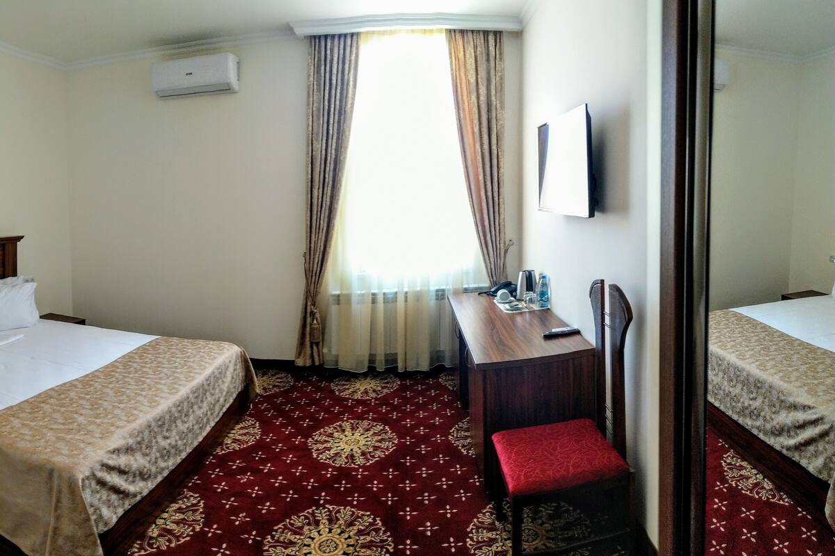 A hotel room with two beds, a desk with a chair, a TV, and a window with curtains.