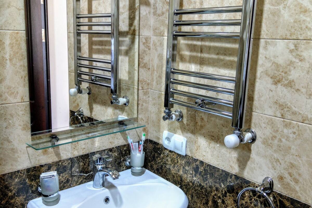 A bathroom with a white sink, a glass shelf above it, a towel hanging on a rack, and a mirror.