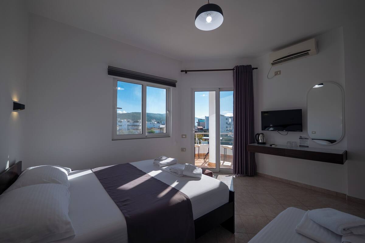 Habitación de hotel con cama, televisor, balcón y vista, y aire acondicionado.