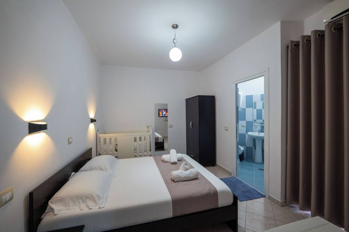 Un hotel moderno con una cama grande, un armario, un baño visible a través de una puerta abierta y vistas de la ciudad.