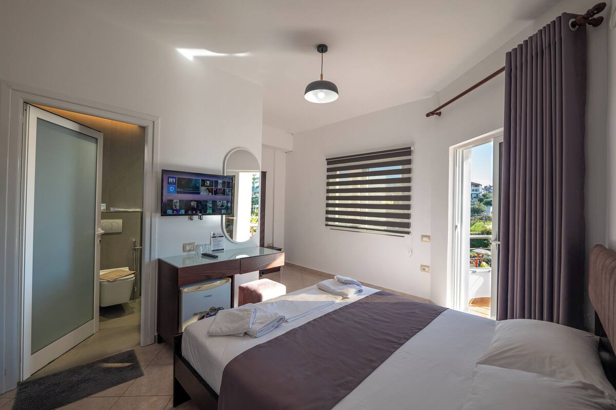 Habitación de hotel con cama, escritorio con computadora, baño y vista al exterior.