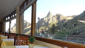 A restaurant with tables and chairs, large windows with a mountain view, and a lamp post outside. - Hotel Rural Imada (Alajero)