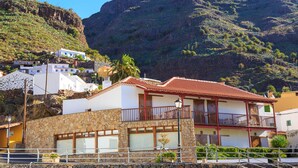 A coastal building with a stone facade, a red-tiled roof, and a balcony with a metal railing. - Hotel Rural Imada (Alajero)