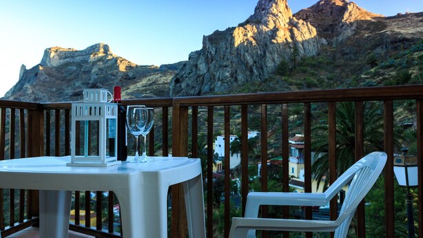 A table with a bottle and glass on a balcony overlooking rocky mountains. - Hotel Rural Imada (Alajero)