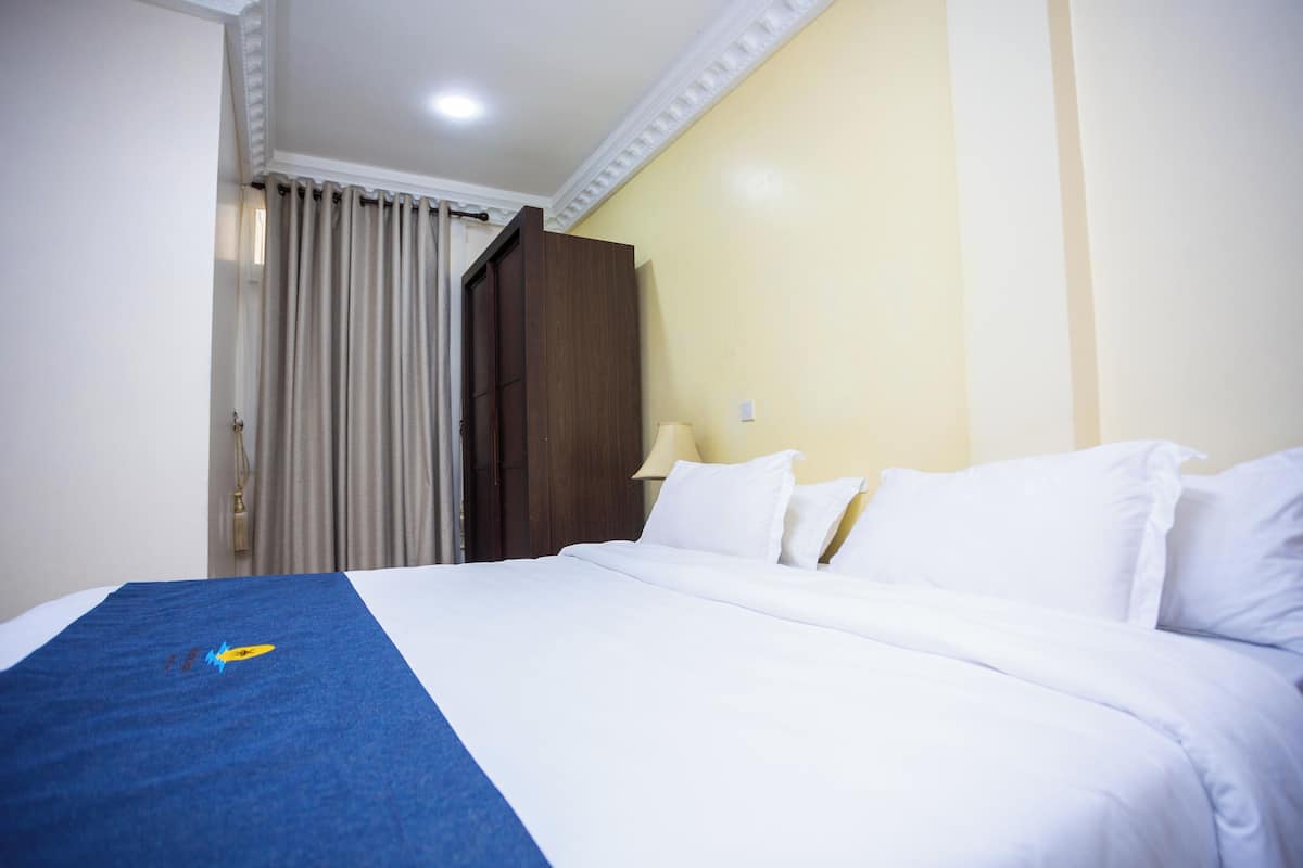 A hotel room with a bed, curtains, a nightstand, and a lamp.