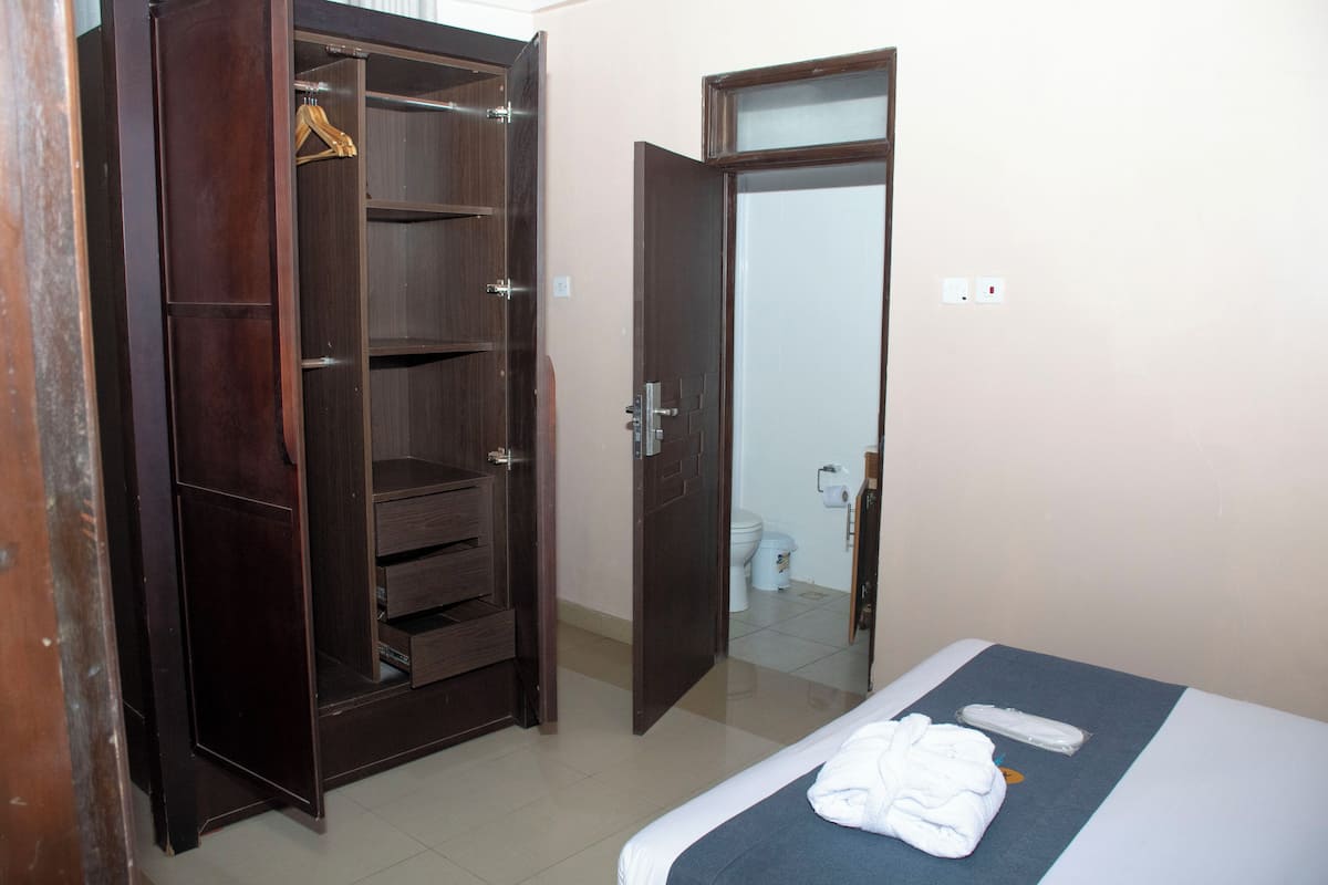 A hotel room with a bed, a wardrobe, and a bathroom visible through an open door.