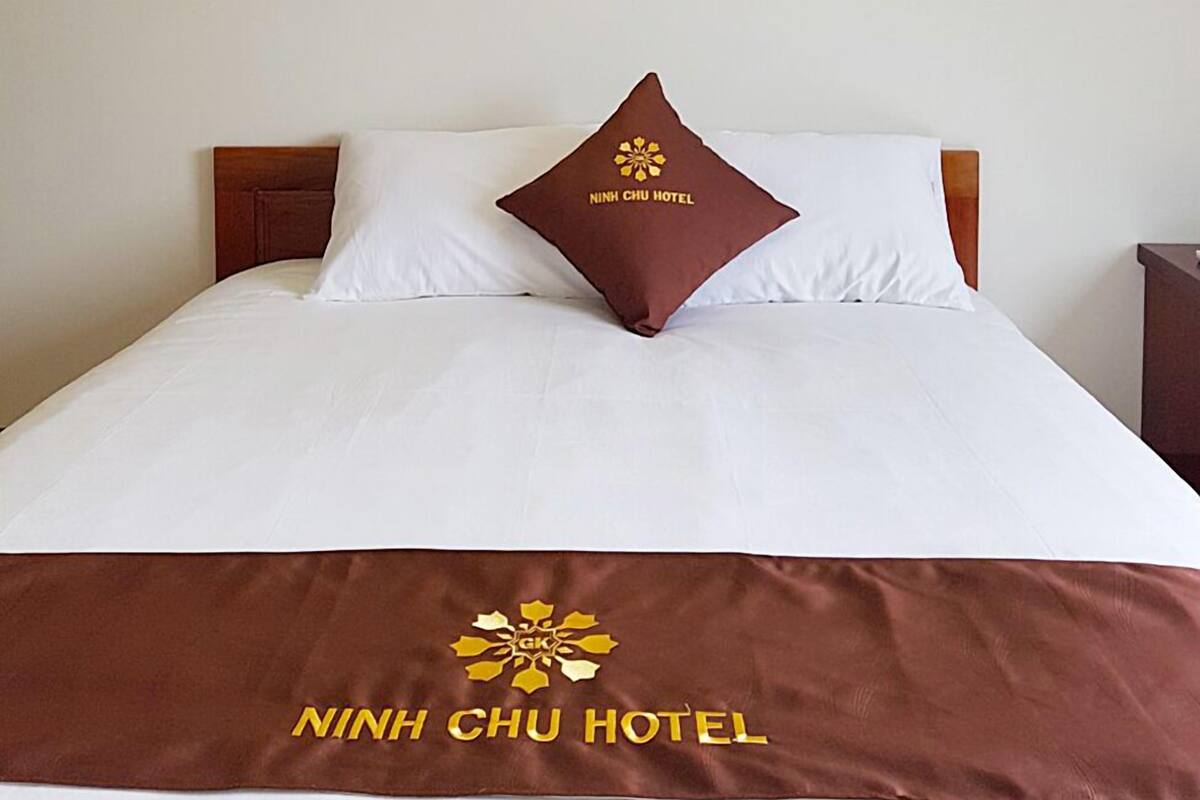 A hotel room with a bed, a pillow with the hotel logo, a framed picture on the wall, and a bedspread with the hotel name.