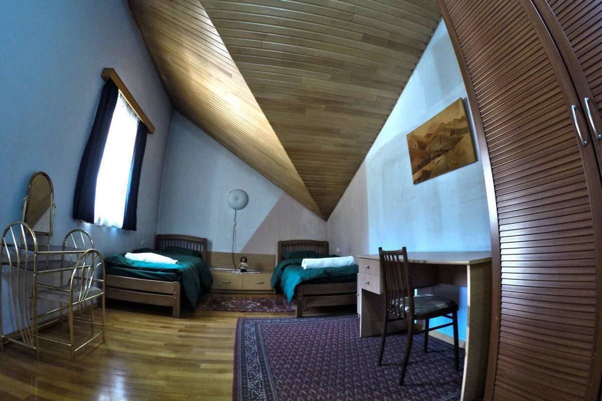 A bedroom with a sloped ceiling, a bed, a desk, a chair, a dresser, and a window.