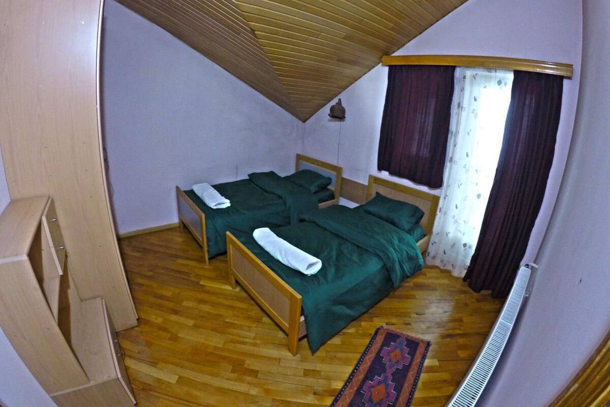 A compact room with two wooden beds, a wooden wardrobe, a radiator, and a window with curtains.