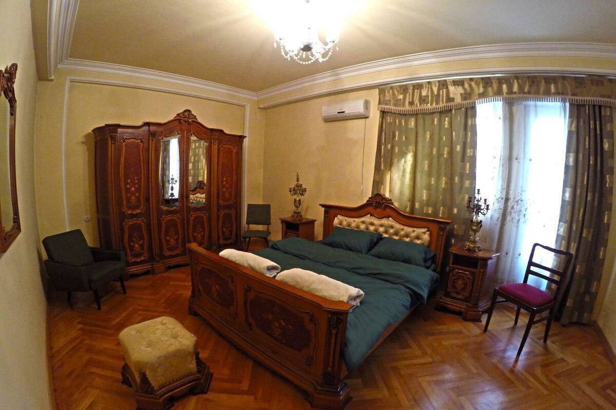 A bedroom with a large bed, a wooden wardrobe, a chair, and a small table.
