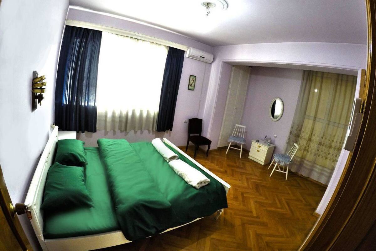 A room with a bed, a chair, a small table, and a mirror.