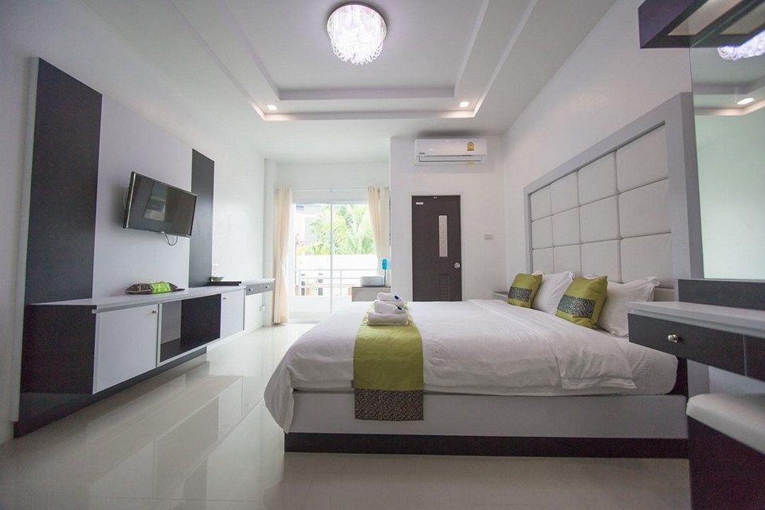 A modern hotel room with a large bed, a flat-screen TV mounted on the wall, and a view of the outdoors through the door.