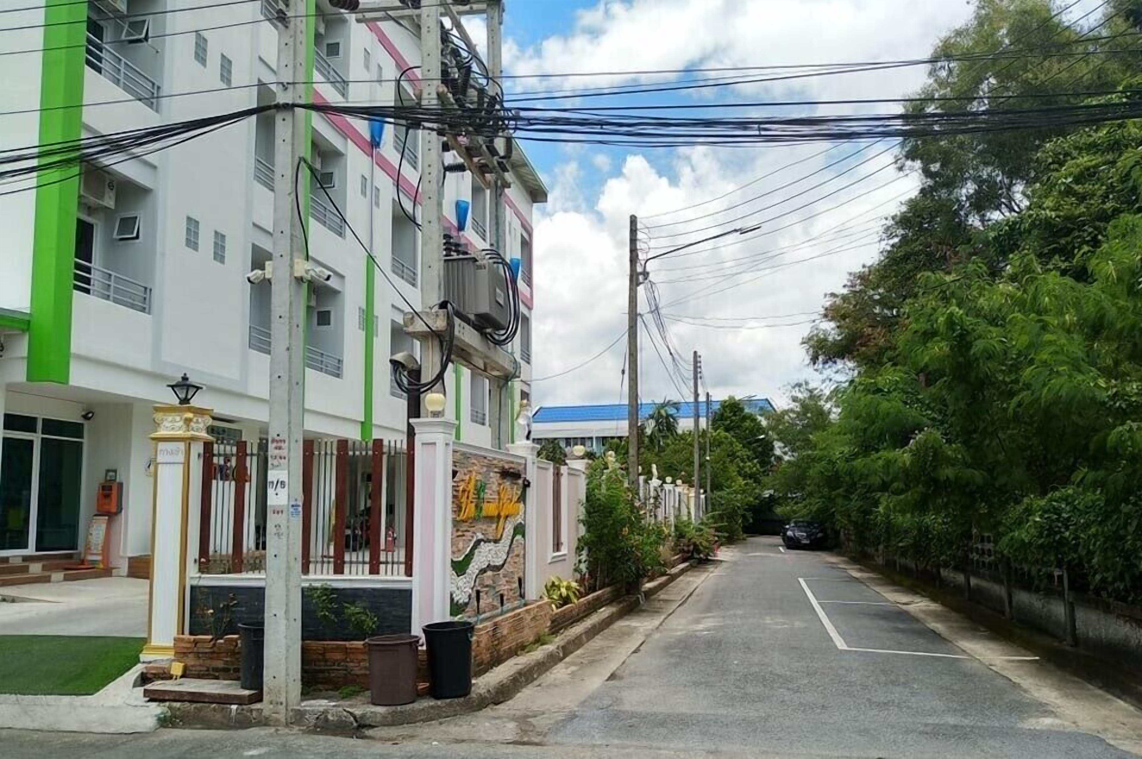 Un immeuble à plusieurs étages, doté d’une façade verte et blanche, orné d  ’une fresque sur le côté, et une rue bordée de voitures garées et d’arbres.